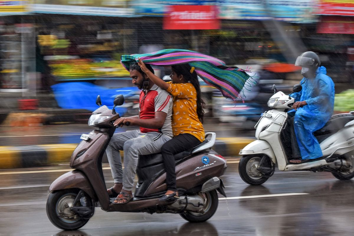 Motorists protect themselves with a scarf while riding a scooter under heavy rain in Bangalore. Credit: AFP Photo