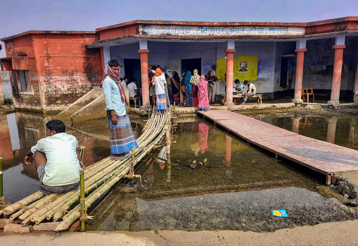 Voters wait to cast their votes at a flooded polling station during the second phase of Assembly elections, at Taraiya in Saran district, Bihar. Credit: PTI Photo
