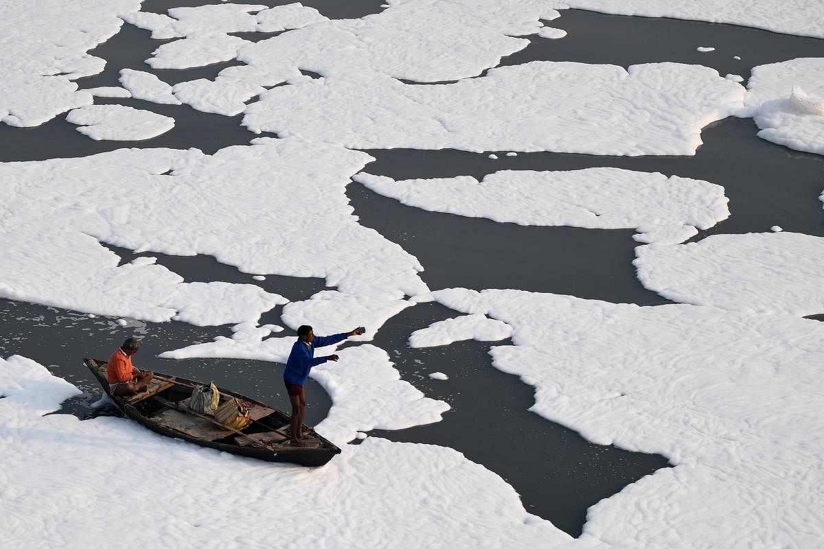 Men row a boat in the polluted waters of river Yamuna covered with foam in New Delhi. Credit: PTI Photo