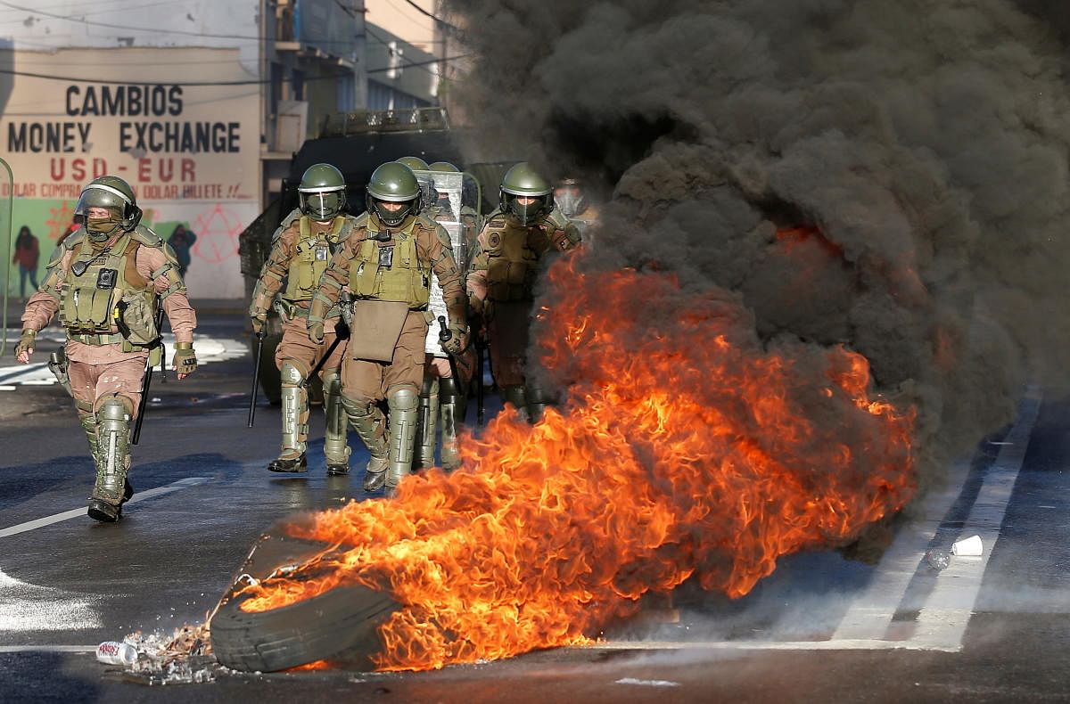 Security forces are seen walking next to tires on fire during a protest against Chile's government in Valparaiso, Chile. Credit: Reuters Photo