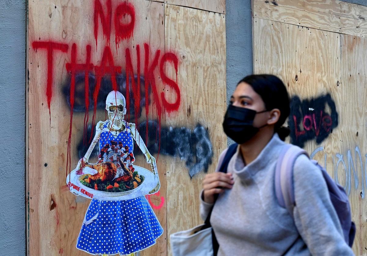 A man walks by street art by @puregenius showing a skeleton holding a tray garnished with a Thanksgiving turkey topped with Coronavirus in New York City. Millions of Americans are ignoring the advice of public health experts and travelling for the Thanksgiving holiday. Credit: AFP Photo