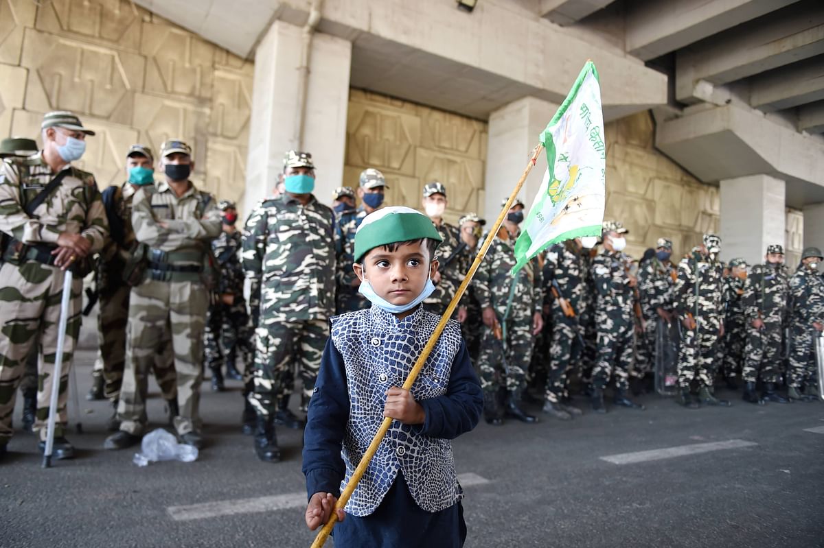 A young boy holds a flag as security personnel stand guard, during the 'Delhi Chalo' protest march by Bharatiya Kisan Union (BKU) members