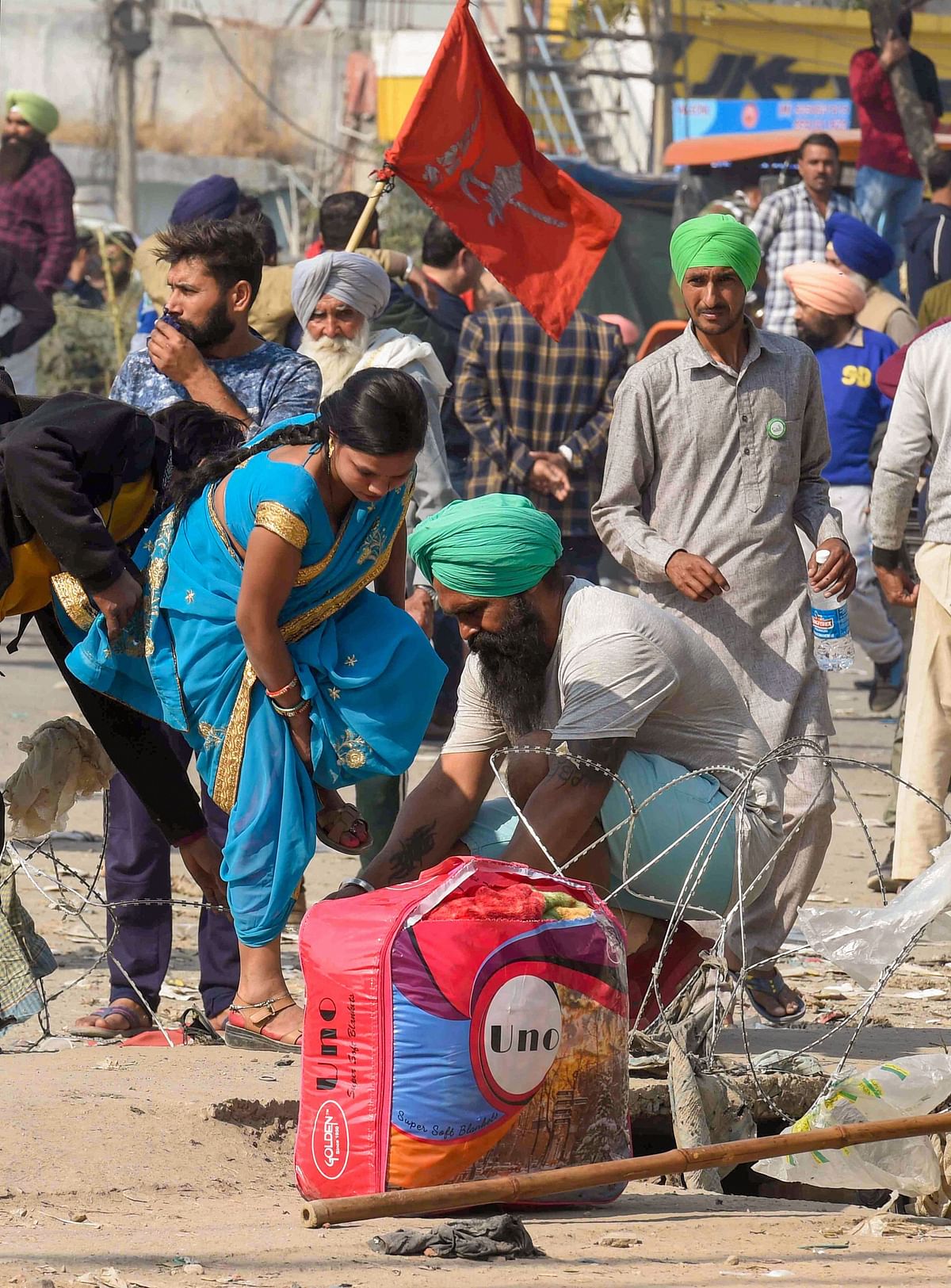 A farmer helps a woman to cross a temporary barricade at Singhu border