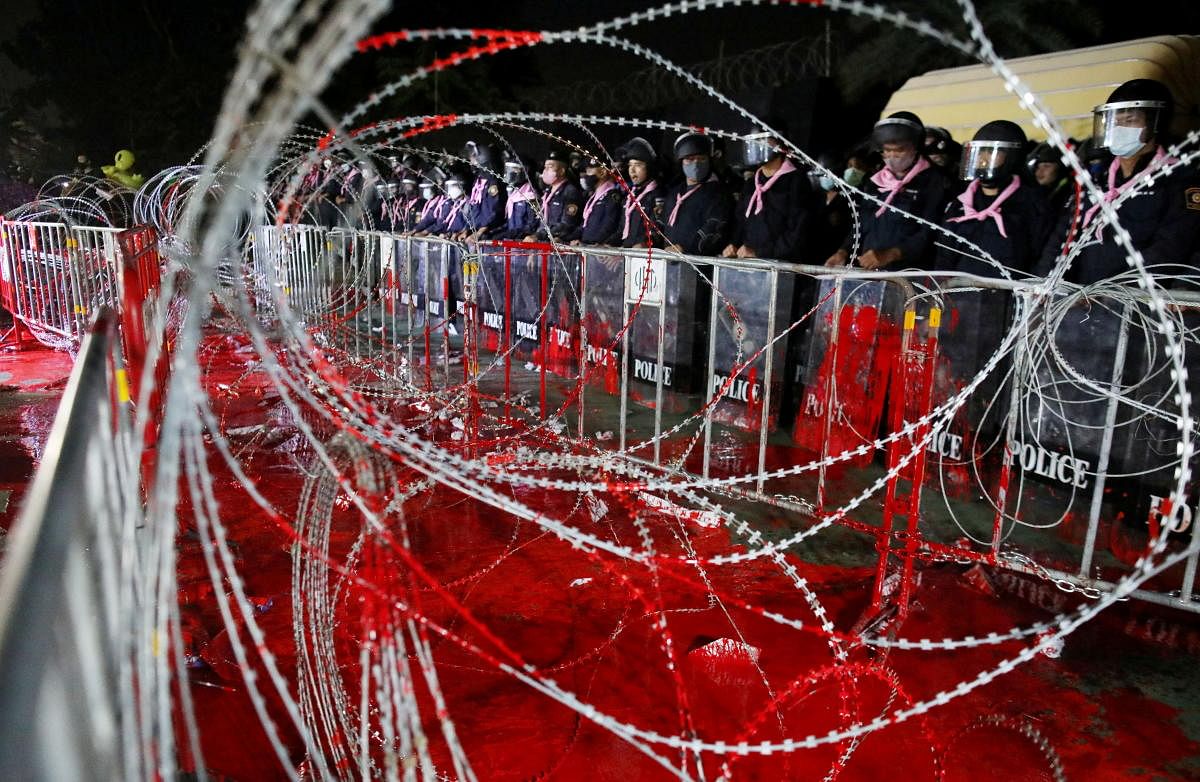 Riot police officers stand guard behind barb wires covered with red paint during a pro-democracy rally demanding Prime Minister Prayuth Chan-ocha to resign and reforms to the monarchy, at 11th Infantry Regiment, in Bangkok, Thailand. Credit: Reuters Photo