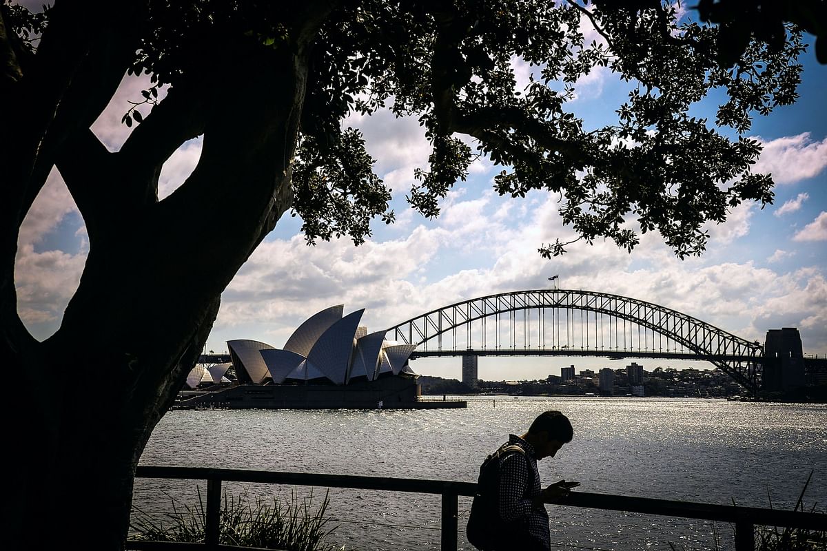 A man looks at photographs he has taken using his phone of the Sydney Opera House and Sydney Harbour Bridge on a Spring day. Credit: AFP Photo