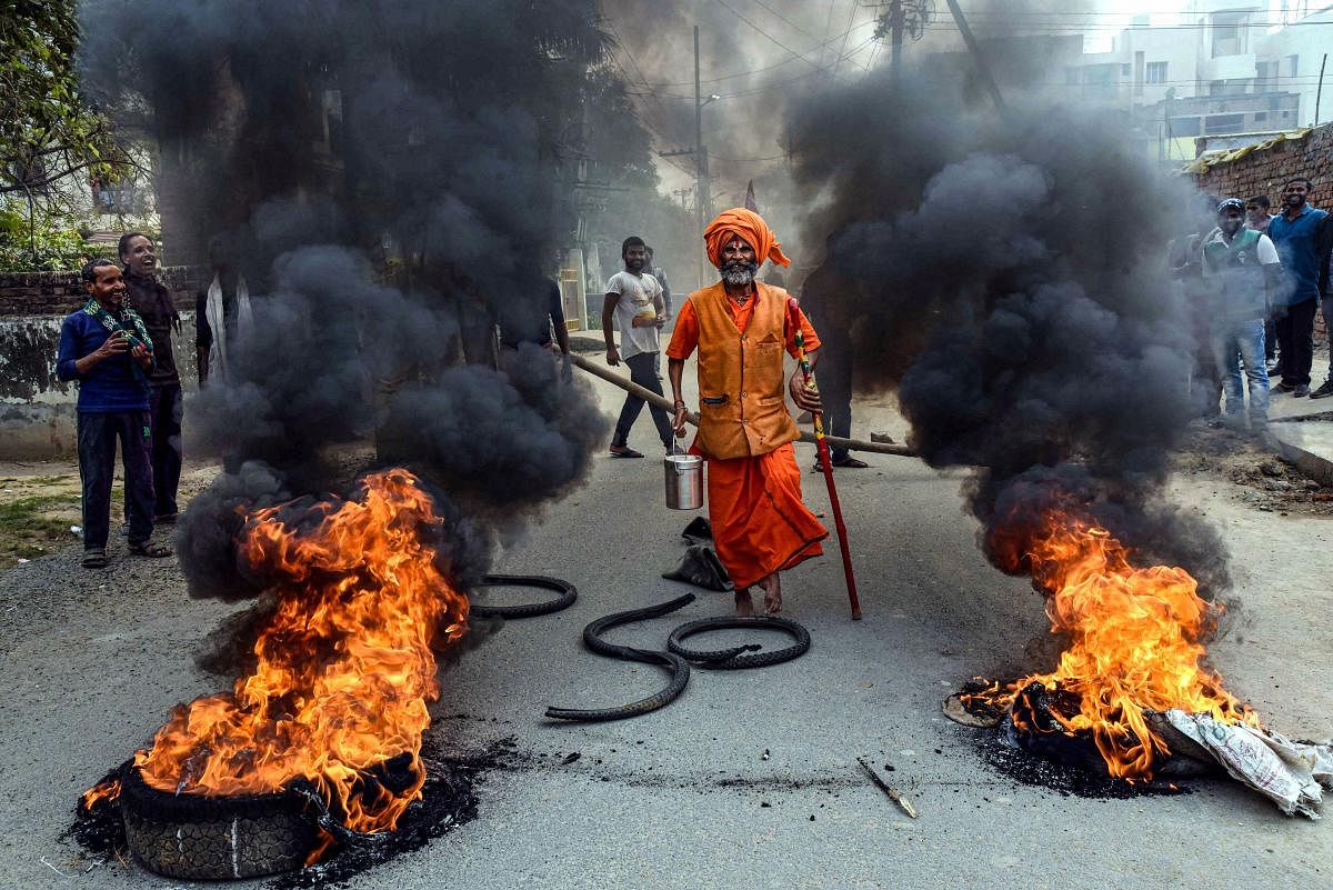 A priest walks past burning tyres, set ablaze by demonstrators in support of the nationwide strike called by agitating farmers against Centre's farm reform laws, in Patna. Credit: PTI Photo.