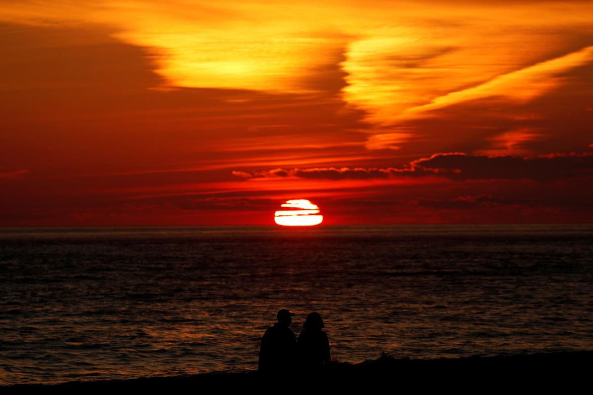 A couple walks on the beach as the sun sets over the Atlantic Ocean at Cape May Point, in Cape May, New Jersey, US. Credit: Reuters