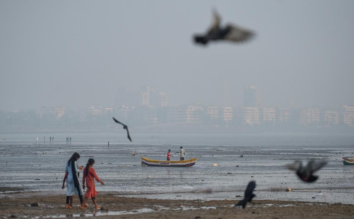 People walk along Girgaum Chowpatty beach as smog engulfs the city skyline. Credit: PTI