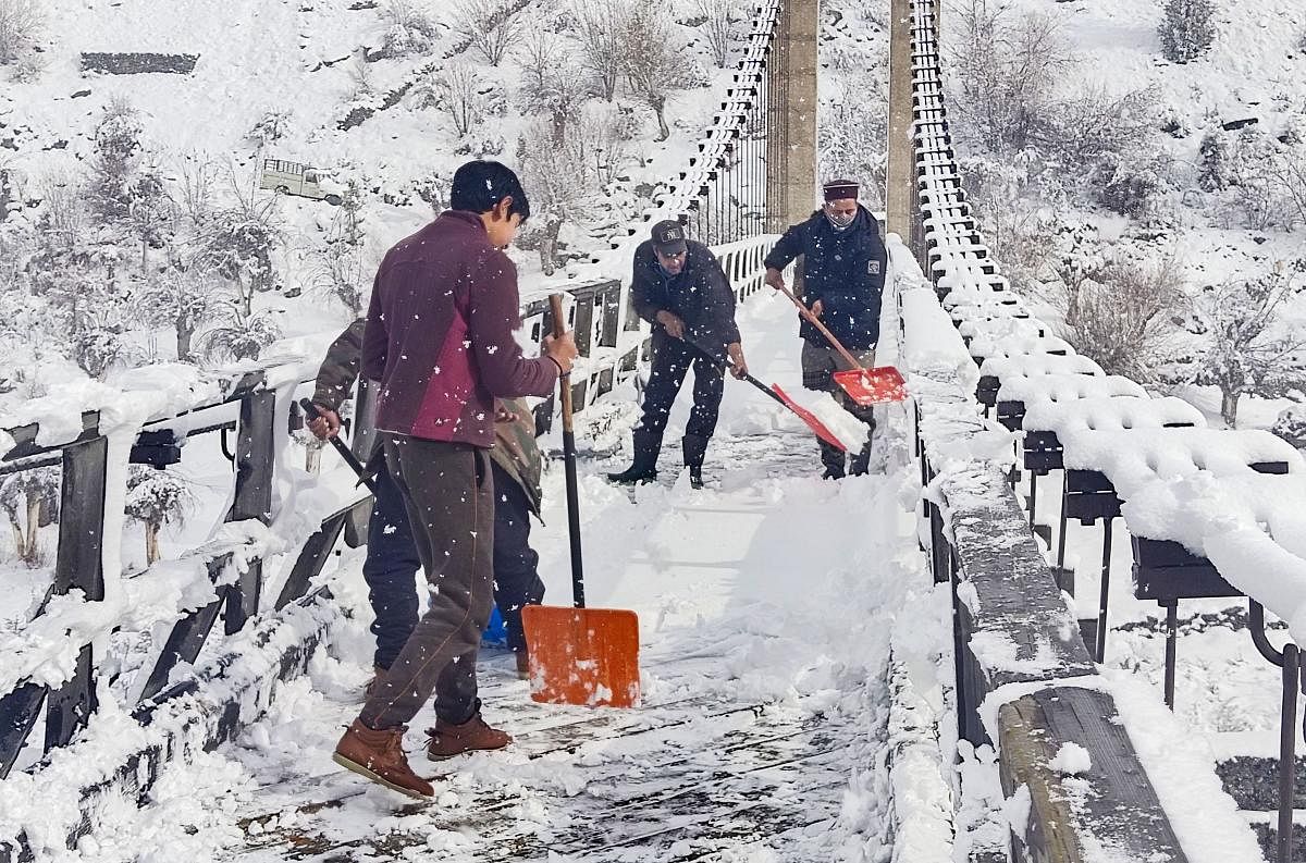 People remove snow from a bridge after the town received fresh snowfall, at Keylong in Lahaul Spiti. Credit: PTI