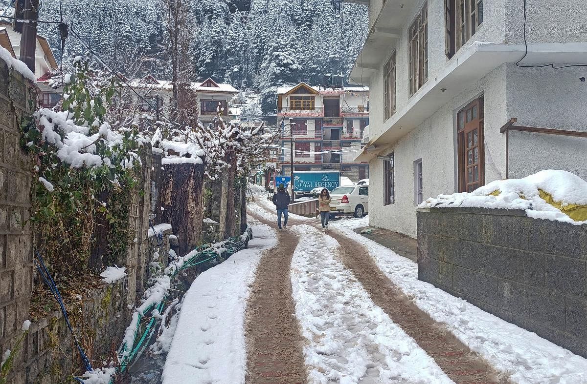 People walk on a snow covered street after the town received fresh snowfall, in Manali. Credit: PTI