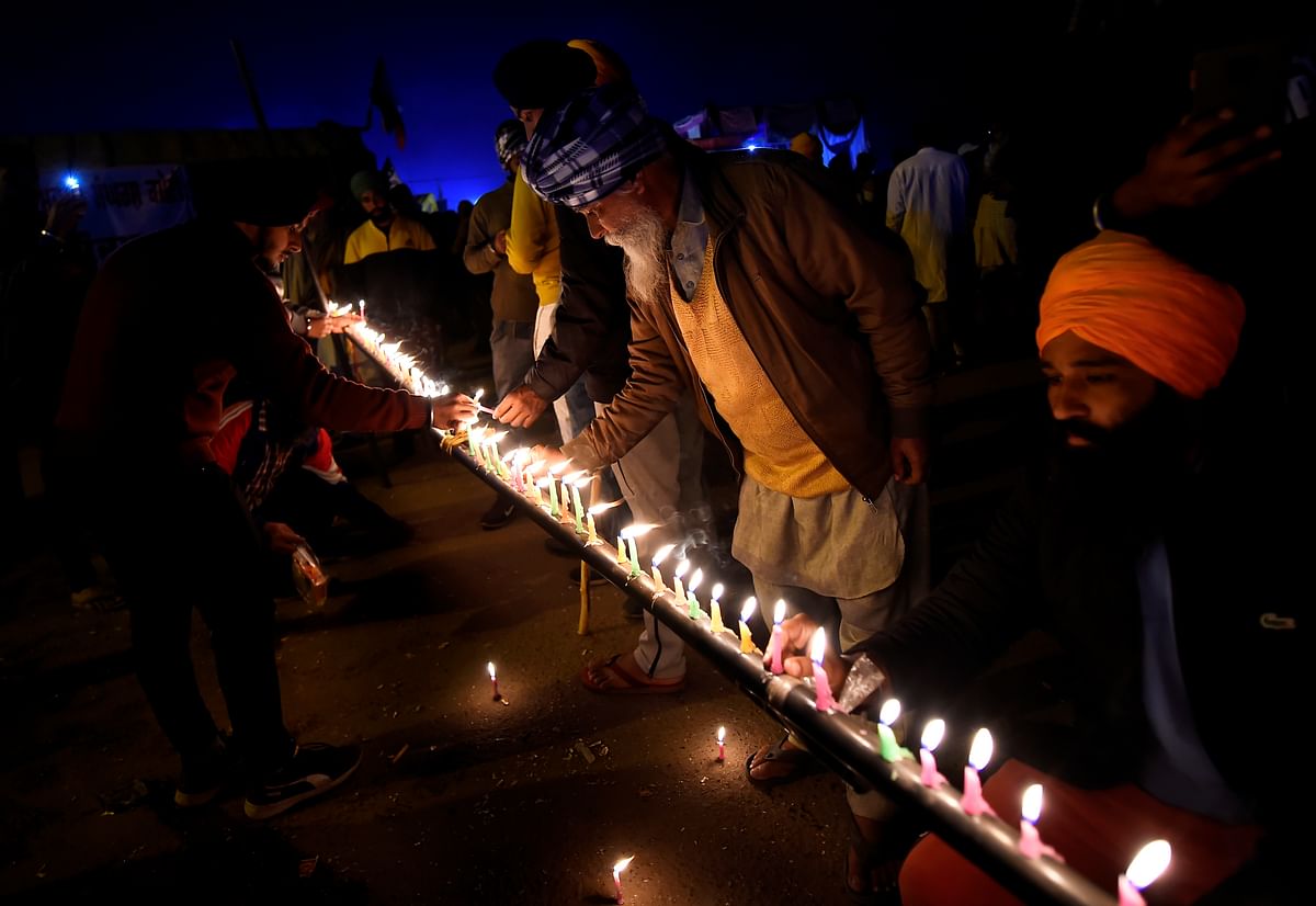 Farmers light candles to pay tribute to those who lost their lives in farmers' agitation, during their sit-in protest against the Centre's farm reform laws, at Singhu border in New Delhi. Credit: PTI Photo