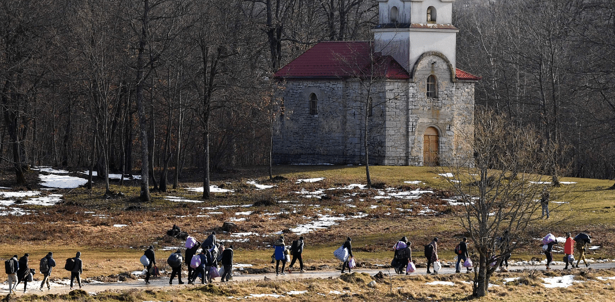 Migrants walk near a church as they leave the migrant camp