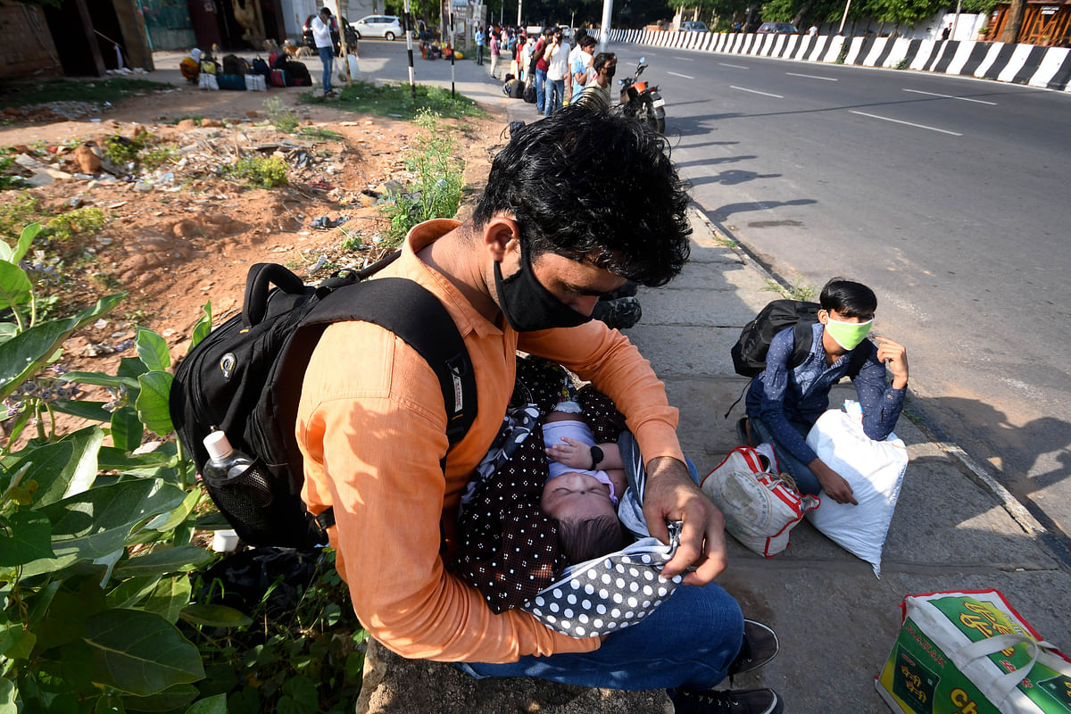The Exodus of migrants | A man holds an infant as several migrant workers travelling to Madhya Pradesh stand in a queue near Palace Grounds, Bengaluru waiting for buses to take them to the railway station. Credit: DH Photo/ Pushkar V