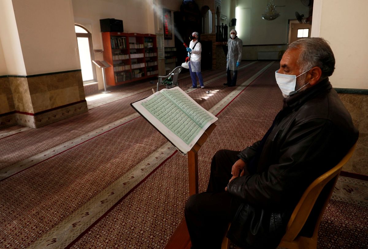A Palestinian reads Koran as a worker disinfects a mosque as a preventive measure against the coronavirus, in Ramallah in the in the Israeli-occupied West Bank. (Credit: Reuters)