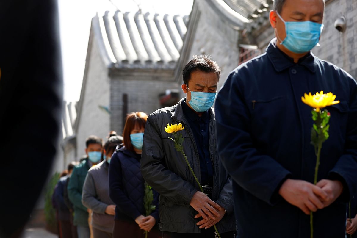 People holding flowers observe a moment of silence at a memorial event in Beijing as China holds a national mourning for those who died of the coronavirus disease (COVID-19), on the Qingming tomb-sweeping festival. (Credit: Reuters)