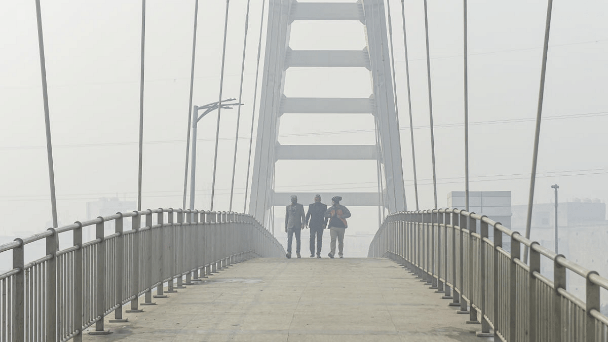 People walk on a foot overbridge, amid dense fog, on a cold morning at Ring Road in New Delhi. Credit: PTI