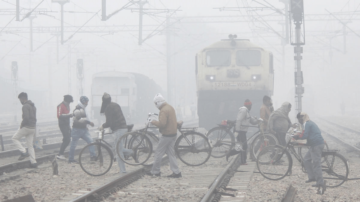 People along with bicycles cross a railway track amid dense fog during a cold winter morning, in Gurugram. Credit: PTI