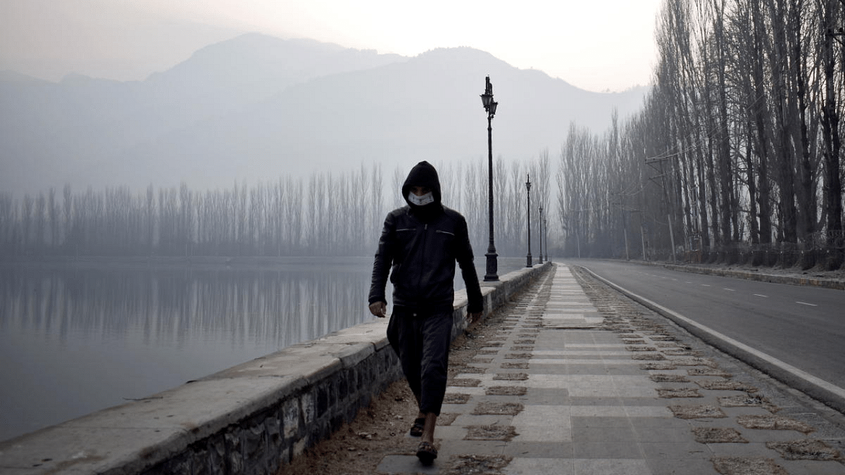 A man wearing a protective face mask walks along the banks of Dal Lake on a cold morning in Srinagar. Credit: Reuters