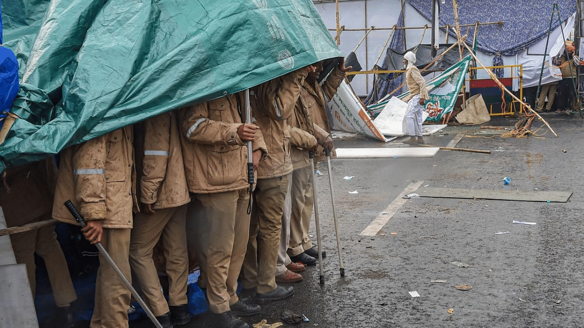 Police personnel take shelter under a tarpaulin sheet during rain near the farmers' protest site at the Delhi-UP border near Ghazipur in New Delhi. Credit: PTI Photo
