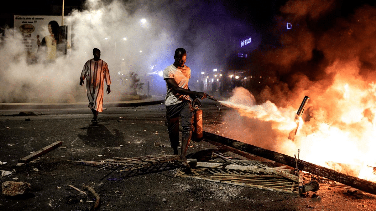 A bystander tries to put out a fire after protest erupted during a curfew in Dakar. Credit: AFP Photo