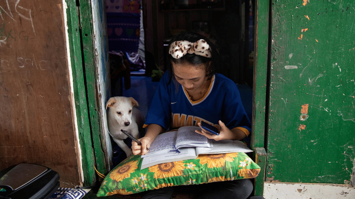 Annie Sabino, 16, a grade 9 student, completes her school work next to her dog, while tending to her family's sidewalk eatery beside their home, as schools remain closed during the Covid-19 outbreak, in Manila, Philippines. Credit: Reuters Photo