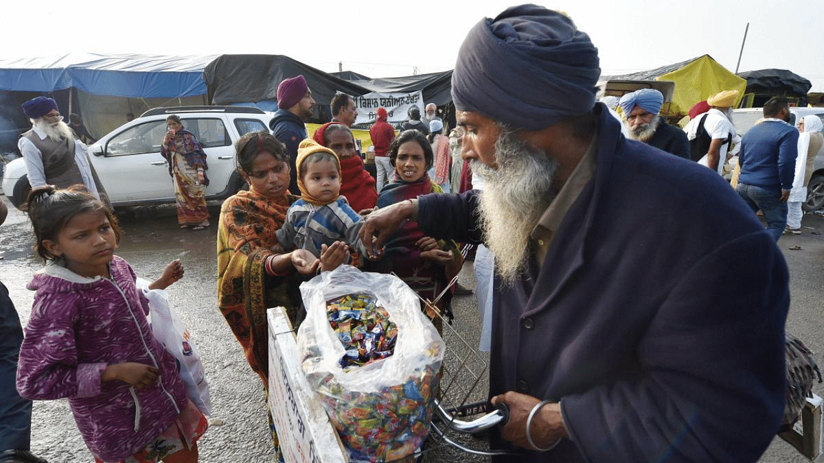 An elderly man distributes toffees among children at Singhu Border during farmers' protest over Centre's farm reform laws, in New Delhi. Credit: PTI Photo