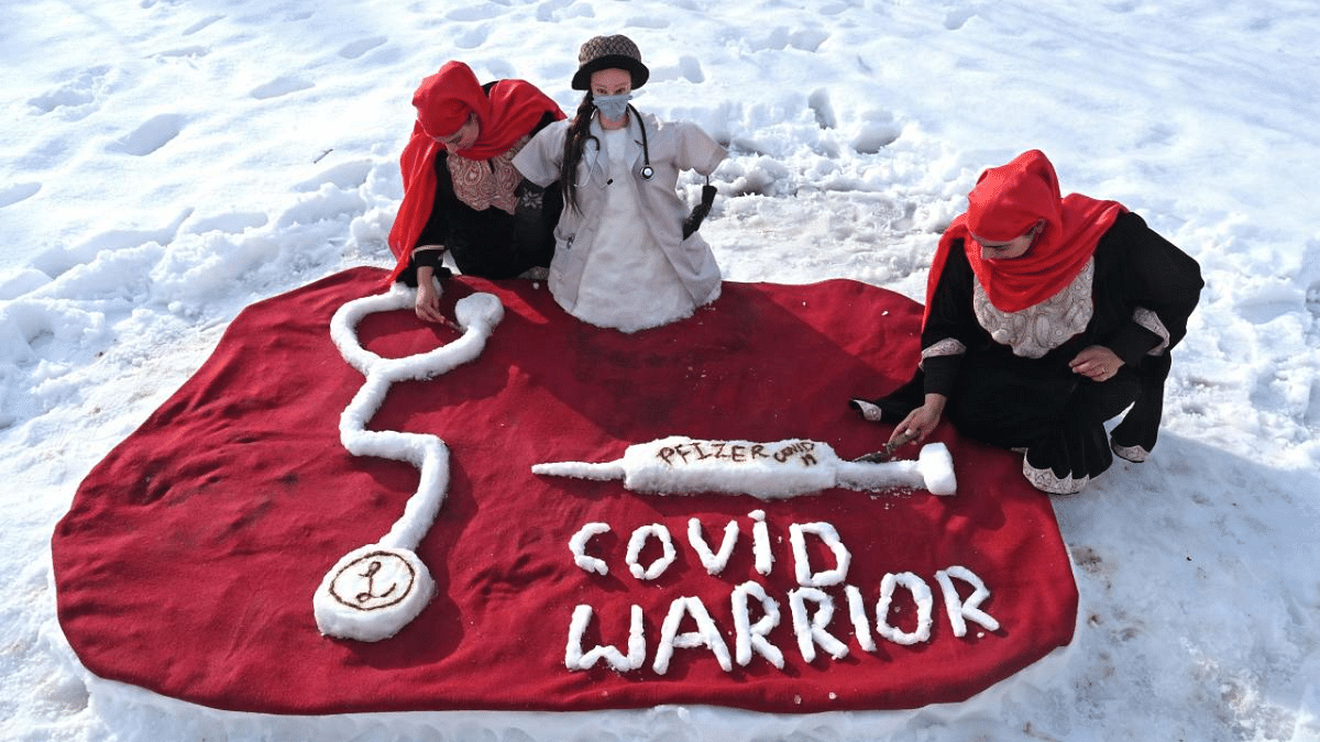 Women make final touches to a snow sculpture of a doctor, a vaccine and a stethoscope made in honour of health workers and their fight against Covid-19 coronavirus, after a heavy snowfall in Srinagar. Credit: AFP Photo
