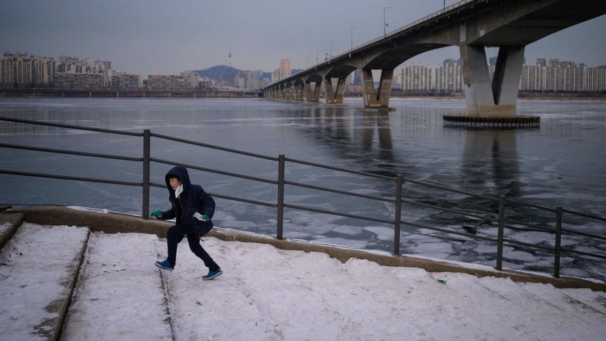 A photo taken on January 10, 2021 shows a child running up steps before a bridge over the frozen Han river and Seoul city skyline. Credit: AFP.