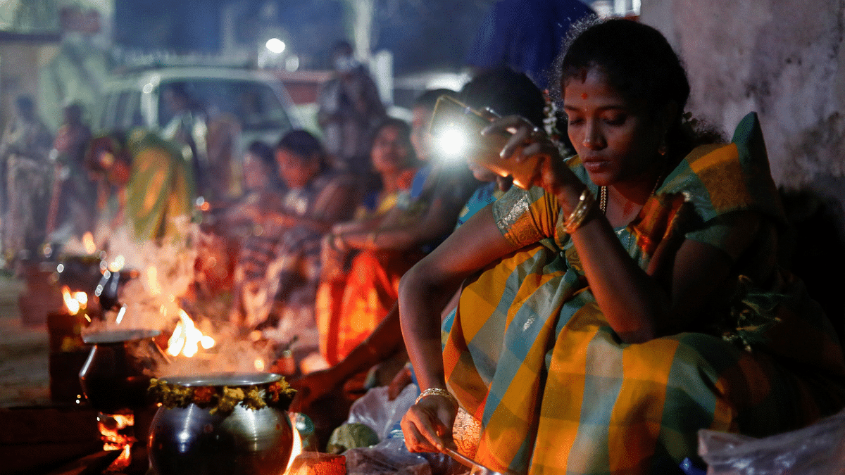 A devotee uses her mobile phone torch as she cooks a rice dish as an offering to the Hindu sun god as devotees attend Pongal celebrations in the early morning at a residential area in Mumbai, India. Credit: AFP Photo
