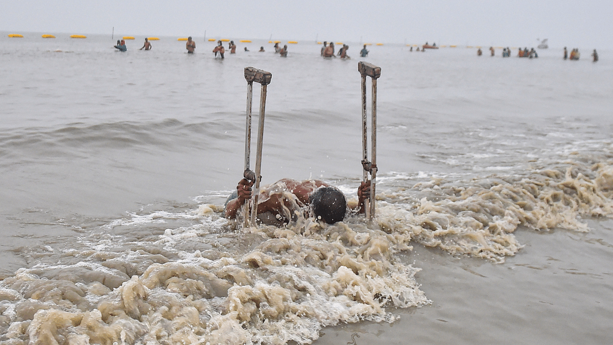 A pilgrim with physical disability takes a holy dip during 'Makar Sankranti' festival celebration at Sagar Island in South 24 Parganas district of West Bengal. Credit: PTI Photo