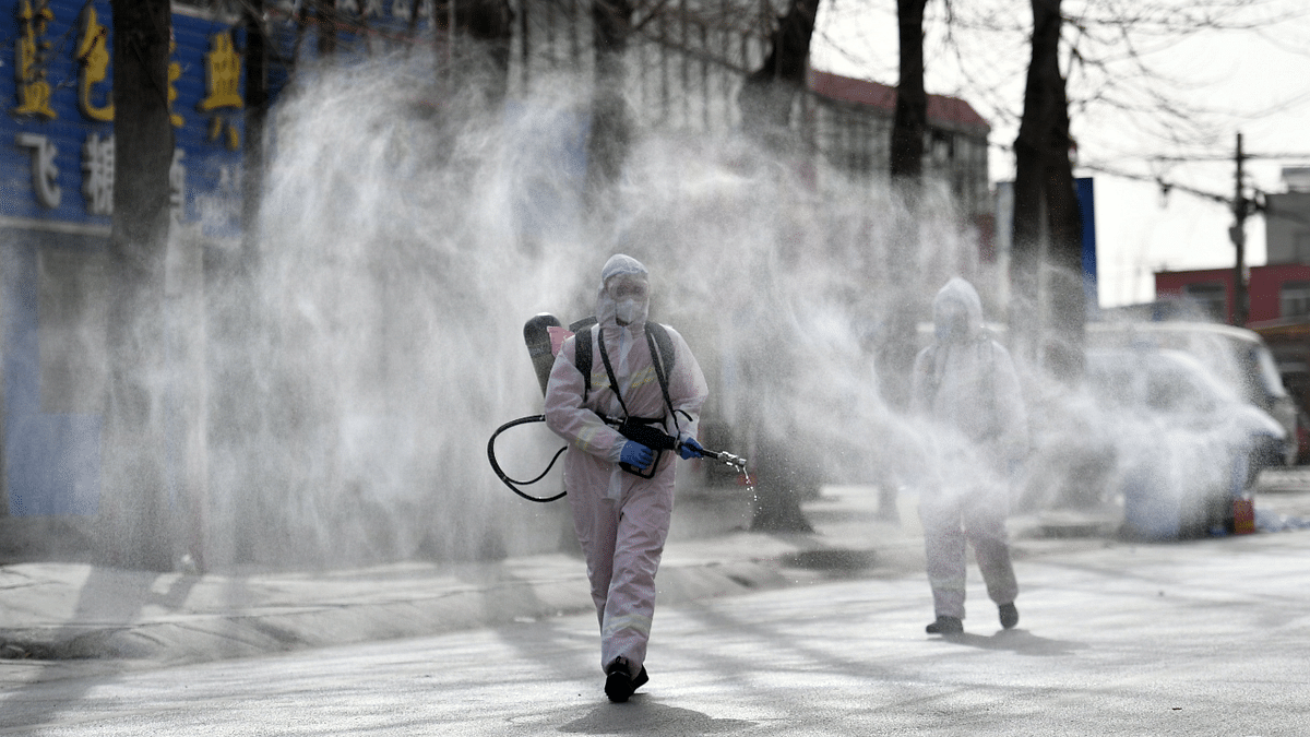 This photo taken on January 15, 2021 shows people in protective suits spraying disinfectant on a street at Gaocheng district, which was declared a high-risk area for Covid-19 in Shijiazhuang, in northern China's Hebei province. Credit: AFP Photo