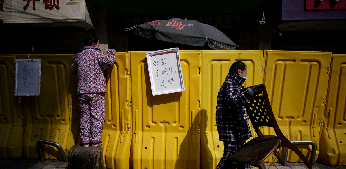 A year since first Wuhan lockdown:  A resident pays for groceries by standing on a tree stump to peer over barriers set up to ring fence a wet market on a street in Wuhan, Hubei province. Credit: Reuters Photo