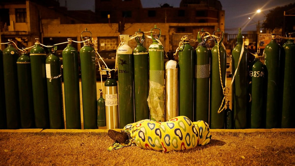 A person sleeps next to empty oxygen tanks to save a spot in the queue, as the supplier refills a tank per person and attends only up to 60 people a day, during the outbreak of Covid-19, in Callao, Peru. Credit: Reuters Photo.