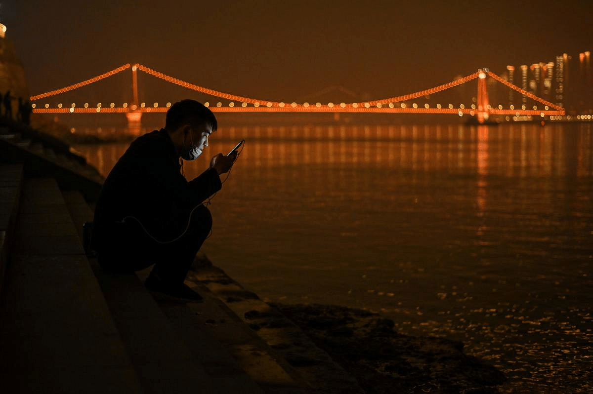 A man looks at his mobile phone as he sits on the banks of the Yangtze River in Wuhan in China's central Hubei province on February 11, 2021, ahead of the start of the Lunar New Year, which ushers in the Year of the Ox. Credit: AFP Photo