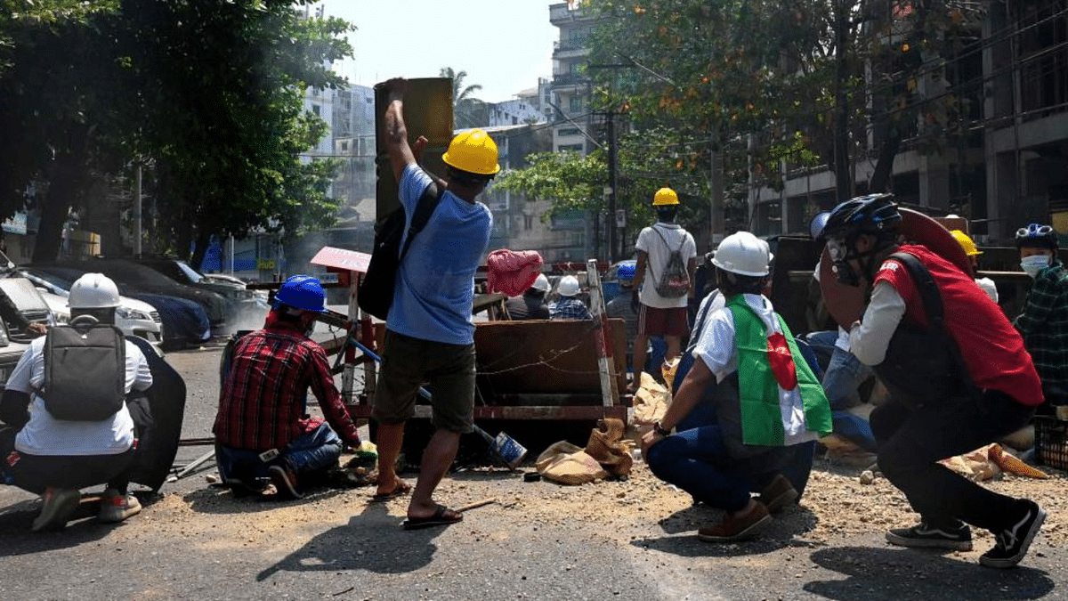 Protesters take cover behind makeshift barricades, made to obstruct security forces, during a demonstration against the military coup in Yangon. Credit: AFP Photo