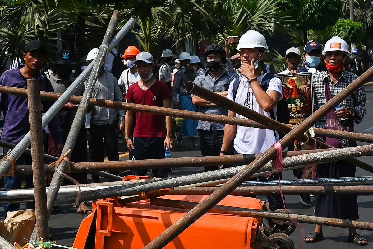 Protesters stand behind makeshift barricades, placed to obstruct security forces, during a demonstration against the military coup in Yangon. Credit: AFP Photo
