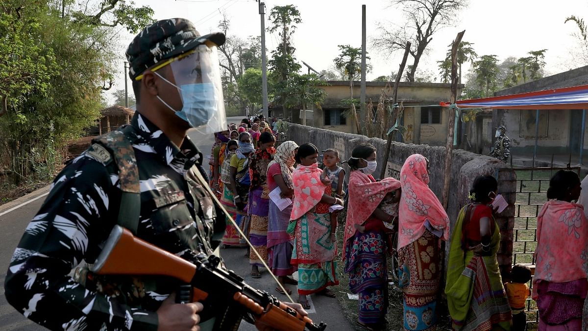 An armed policeman wearing a face shield stands guard as women wait in line to cast their votes outside a polling booth during the first phase of the West Bengal state election in Purulia district. Credit: Reuters Photo