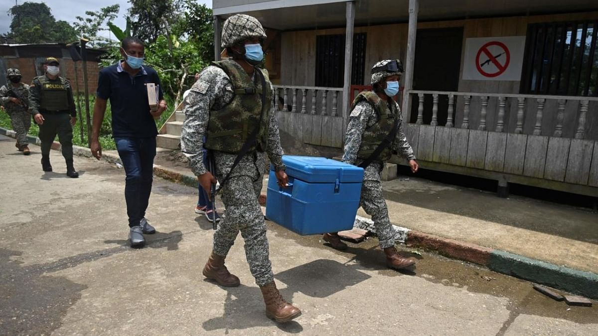 Colombian soldiers navy carry a cooler with doses of the CoronaVac vaccine -developed by China's Sinovac laboratory- against the Covid-19 disease, in Santa Genoveva de Docordo, rural area of the municipality of Litoral del San Juan, Choco department, Colombia. Credit: AFP.