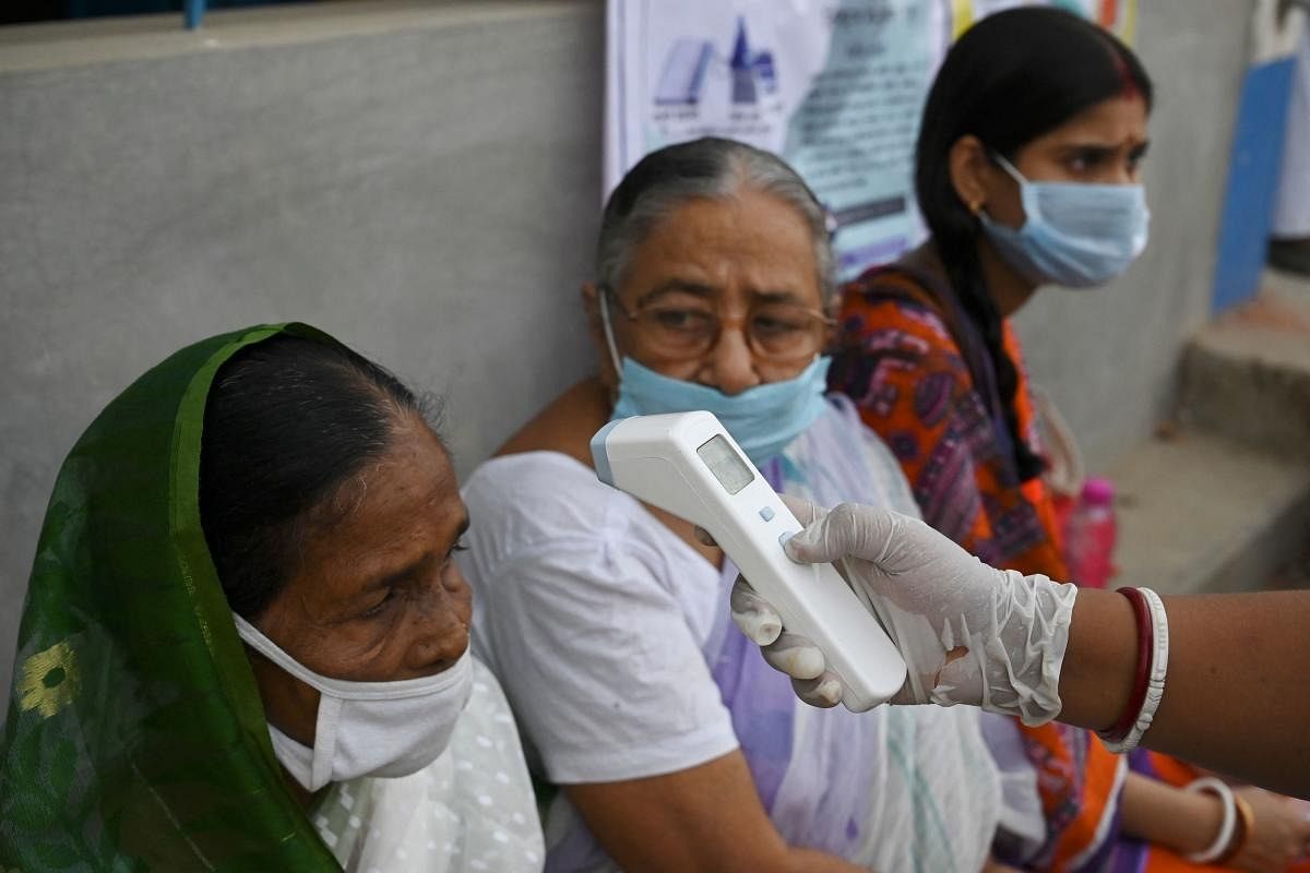 A volunteer checks the body temperature of a voter before entering a polling station to cast her vote during Phase 2 of West Bengal's legislative election in Nandigram. Credit: AFP Photo