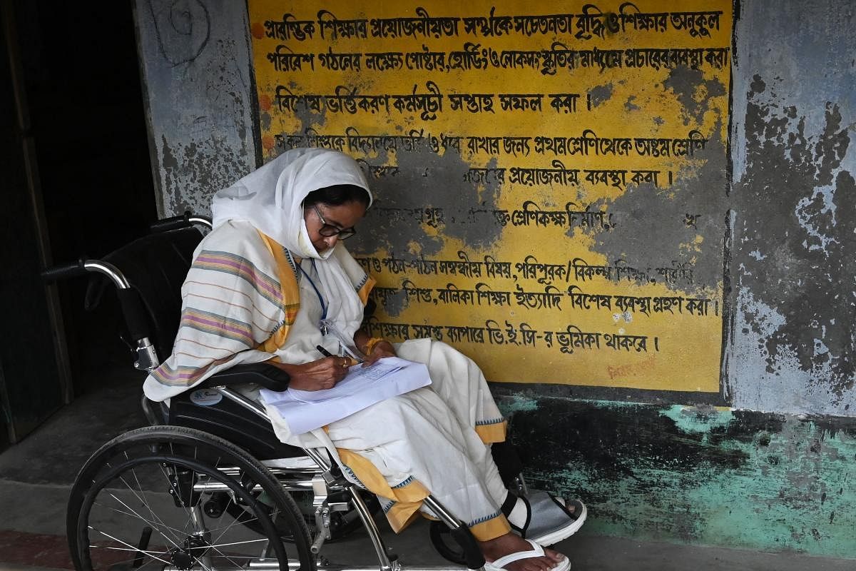 West Bengal's Chief Minister Mamata Banerjee takes notes while sitting in a wheelchair at a polling station during Phase 2 of West Bengal's legislative election in Nandigram. Credit: AFP Photo