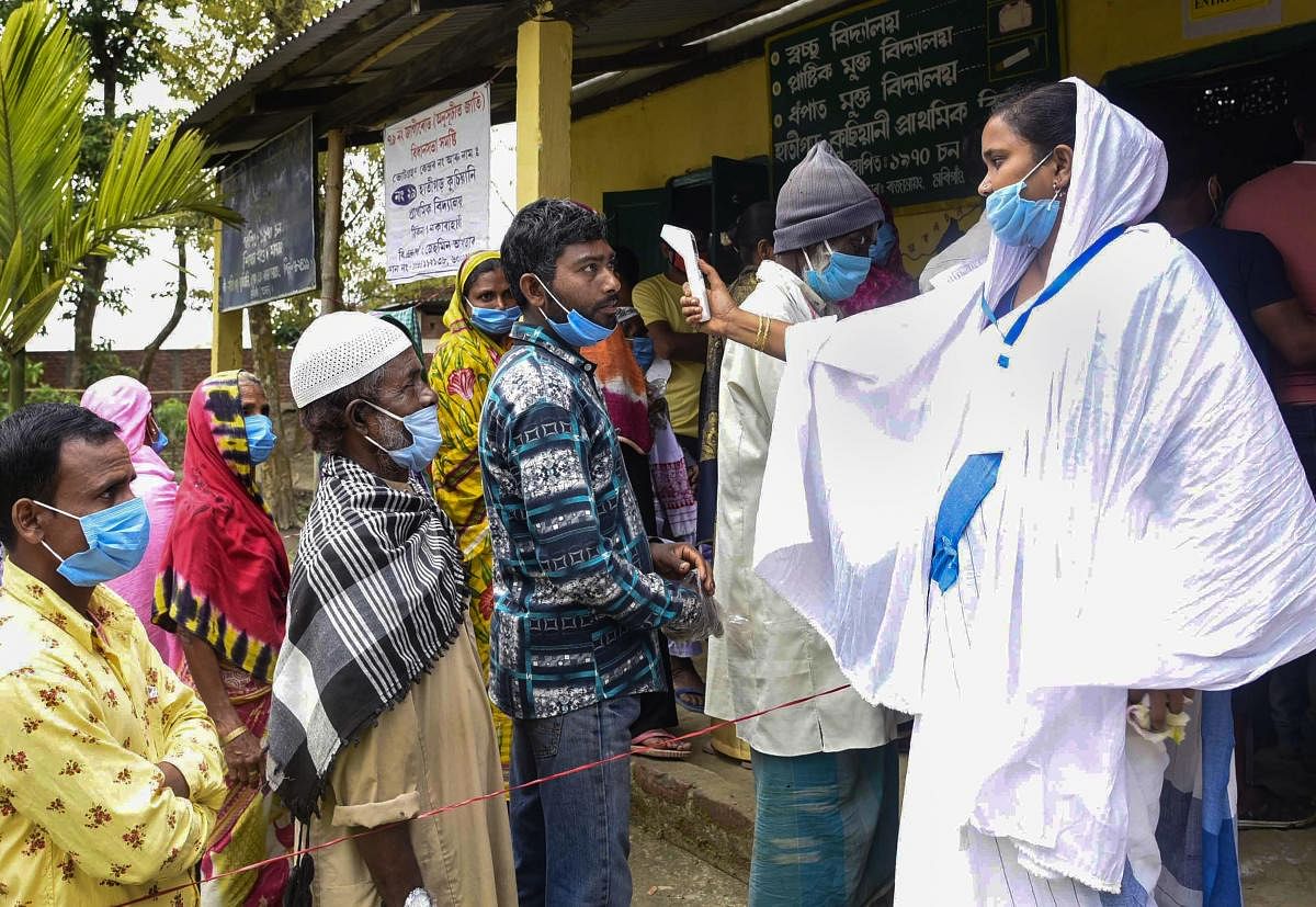 Voters undergo thermal screening as they arrive to cast their votes during the second phase of the Assam Assembly election, at a polling station in Morigaon district. Credit: PTI Photo