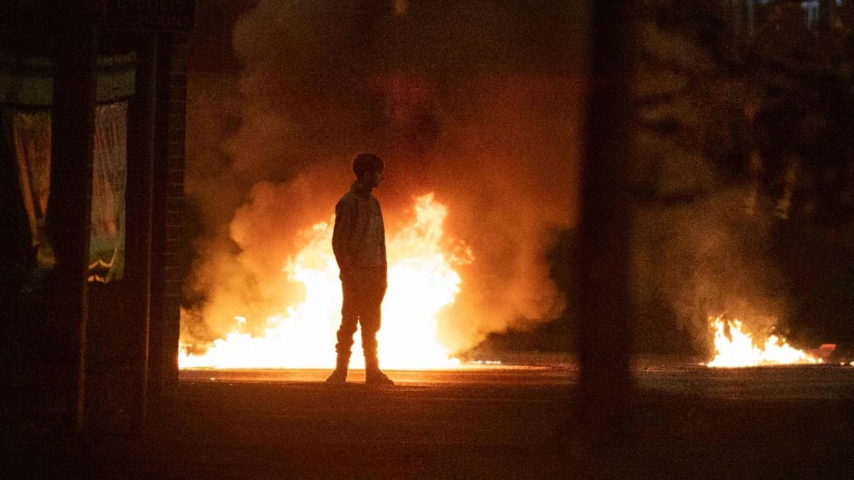 A boy stands and looks on as flames and smoke rises behind him at the scene of violence in Newtownabbey, north of Belfast, in Northern Ireland. Credit: AFP Photo