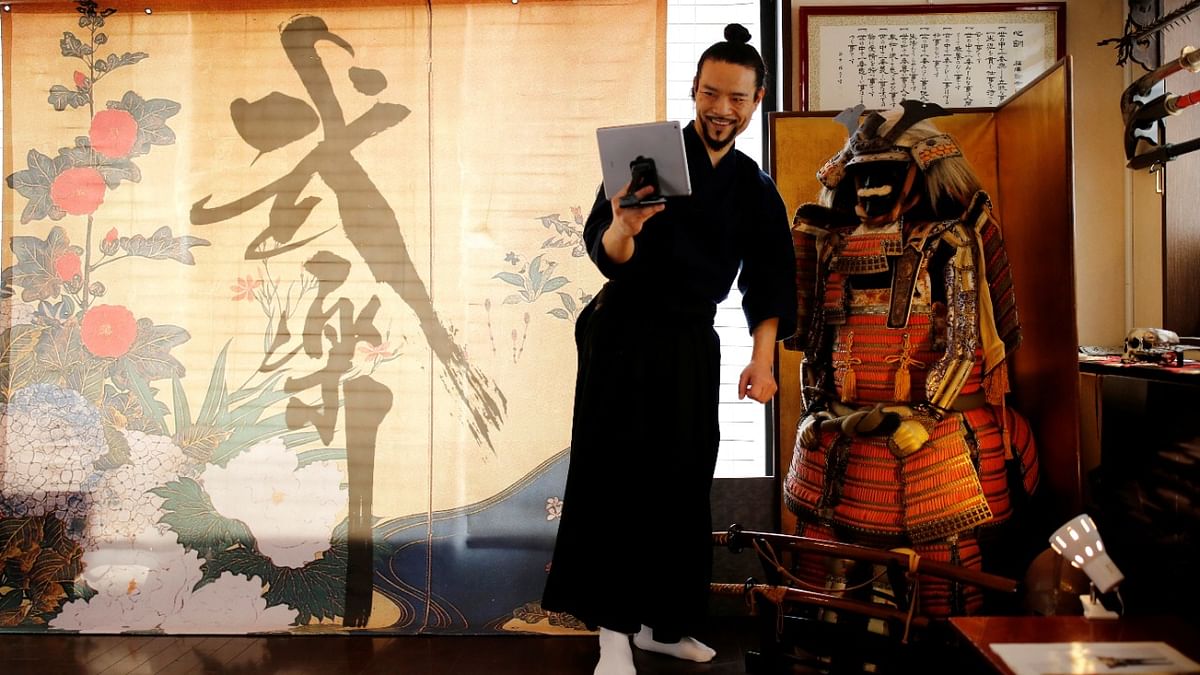 The founder of Bugaku and Samurai martial arts instructor Koshiro Minamoto holds a tablet as he shows his students a Samurai armor during an online class for Samurai experience in Tokyo, Japan. Credit: Reuters Photo