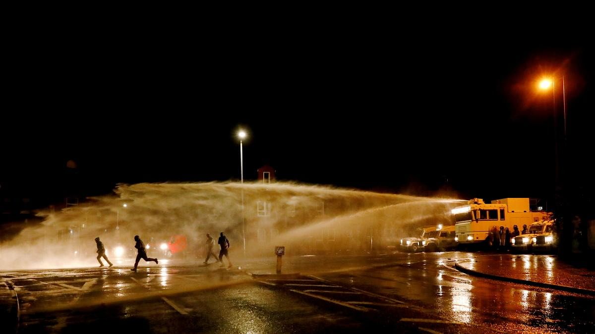 Rioters react as the police uses a water cannon on the Springfield Road as protests continue in Belfast, Northern Ireland. Credit: Reuters Photo