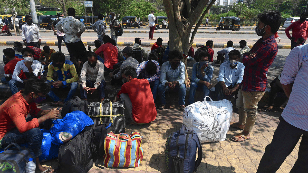 A group of migrant workers wait under the shade of a tree outside Lokmanya Tilak Terminus railway complex to catch a train back home ahead of the harvest season amidst rising Covid-19 coronavirus cases in Mumbai. Credit: AFP Photo