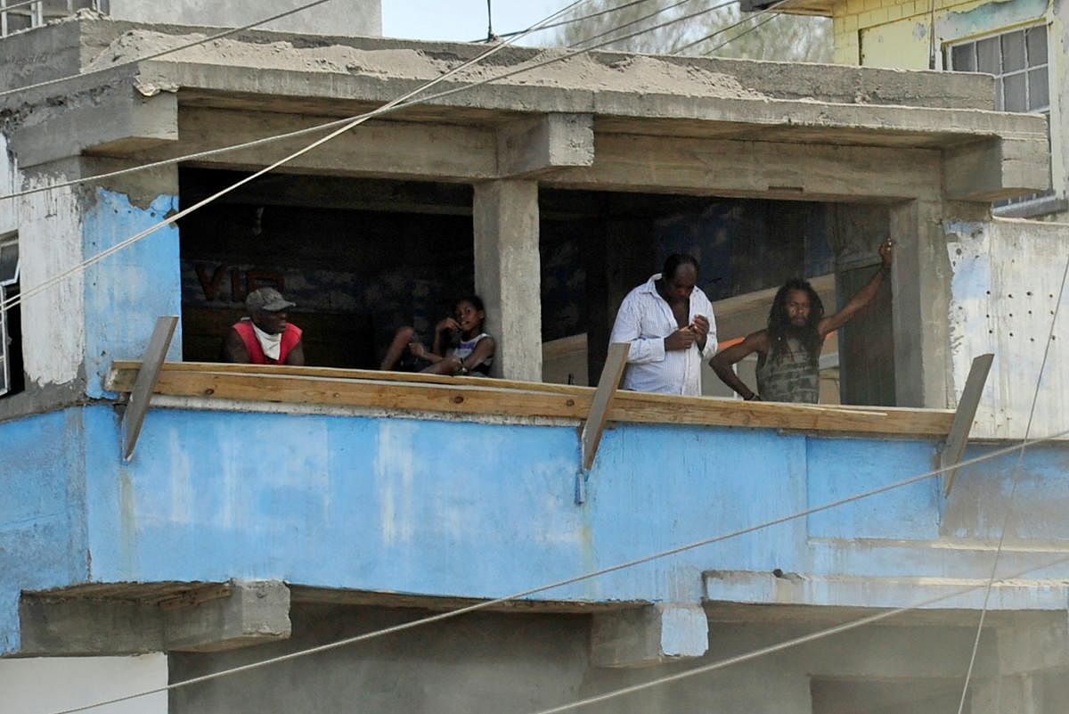 People stand in the balcony of an ash covered house after a series of eruptions from La Soufriere volcano in Sandy Bay, Saint Vincent and the Grenadines. Credit: Reuters photo.