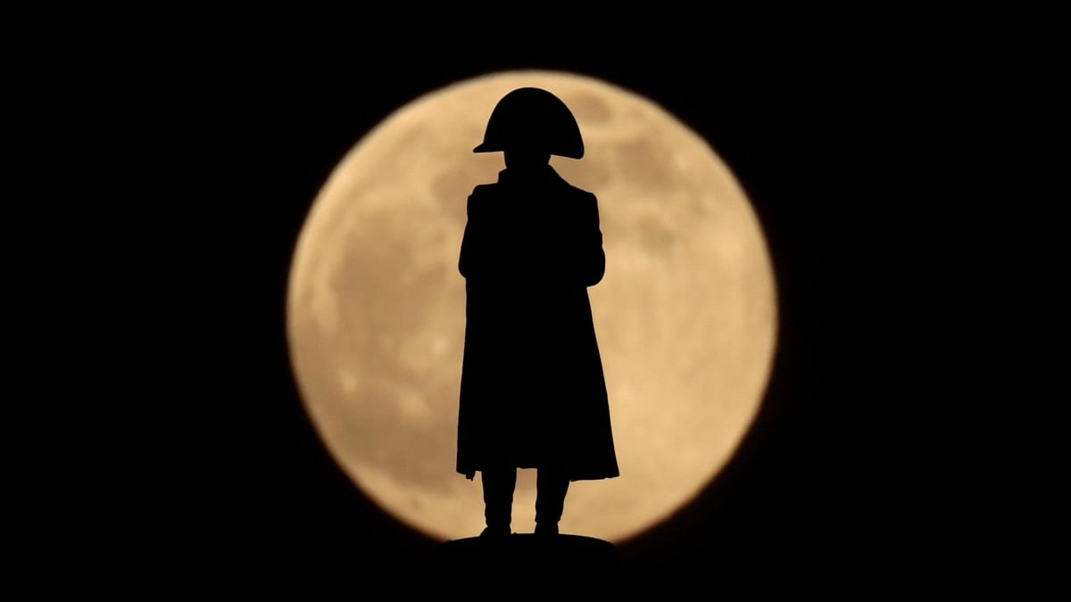 The statue of Napoleon I in chasseur uniform (1962) by French sculptor Pierre Stenne, atop the Column of the Grande Armee, is silhouetted in front of a full moon, known as the