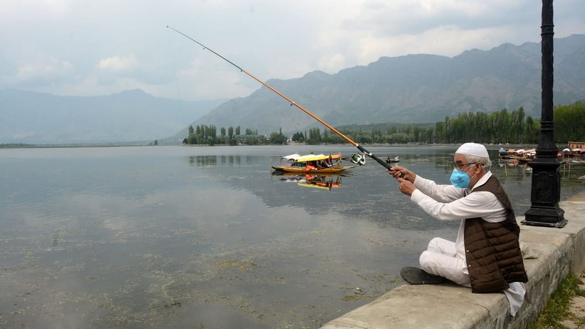 An elderly man wearing a face mask enjoys fishing at Dal Lake.