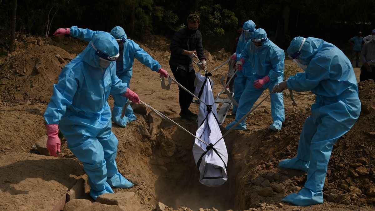 Relatives wearing personal protective equipment (PPE) suits lower the body of a Covid-19 coronavirus victim during the burial at a graveyard in New Delhi. Credit AFP Photo