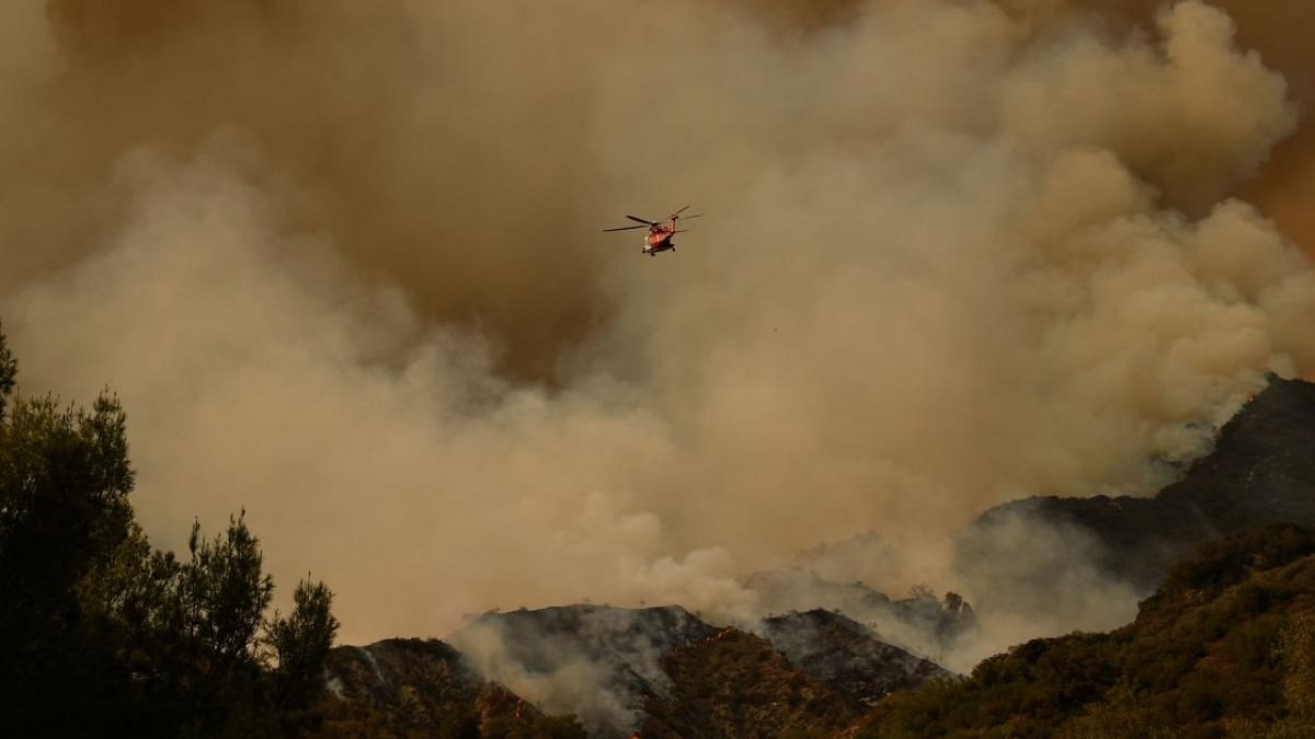 A helicopter is seen flying above the plume of smoke created by the Palisades fire in Topanga State Park, North West of Los Angeles. Credit: AFP Photo